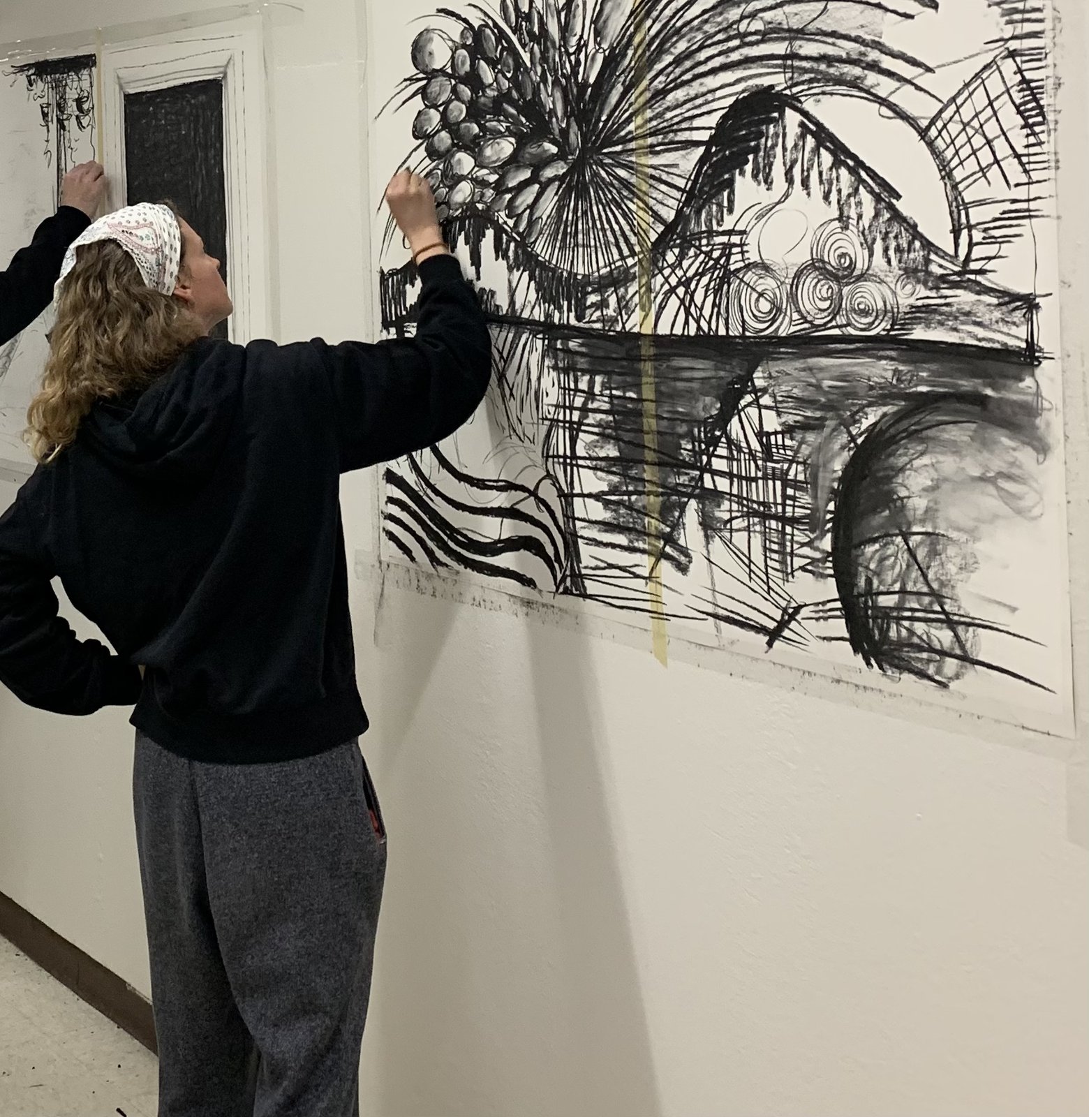 Adults working on large charcoal drawings taped to a studio wall